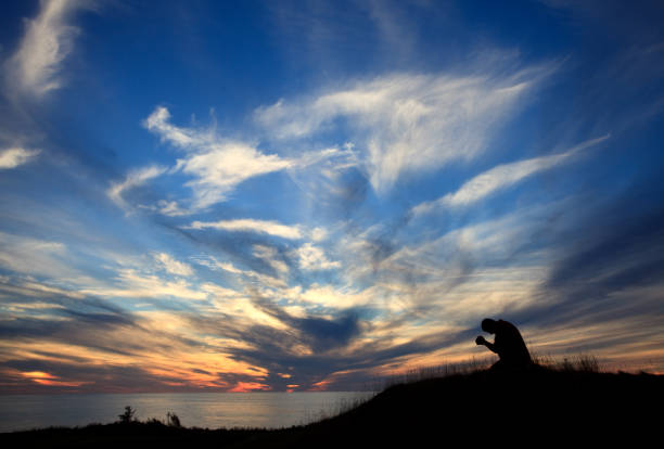 sylwetka człowieka na kolanach w modlitwie przez ocean przed pięknym zachodem słońca niebo - praying men god kneeling zdjęcia i obrazy z banku zdjęć