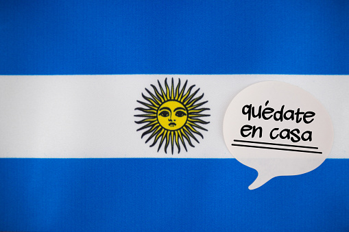 White Speech Bubble Note Paper With Stay Home Message In Spanish language On The Argentinian Flag. Horizontal composition with copy space.