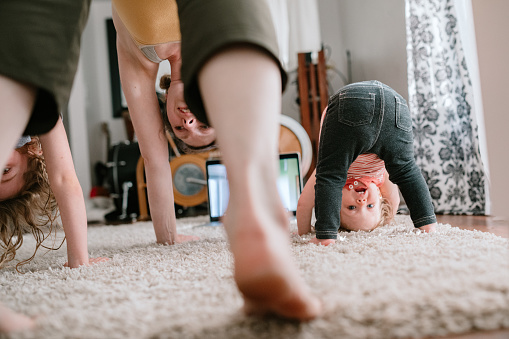 A mother does a virtual exercise class with her daughters in their living room.  Part of the regular routine or the new normal with social distancing and Covid-19.