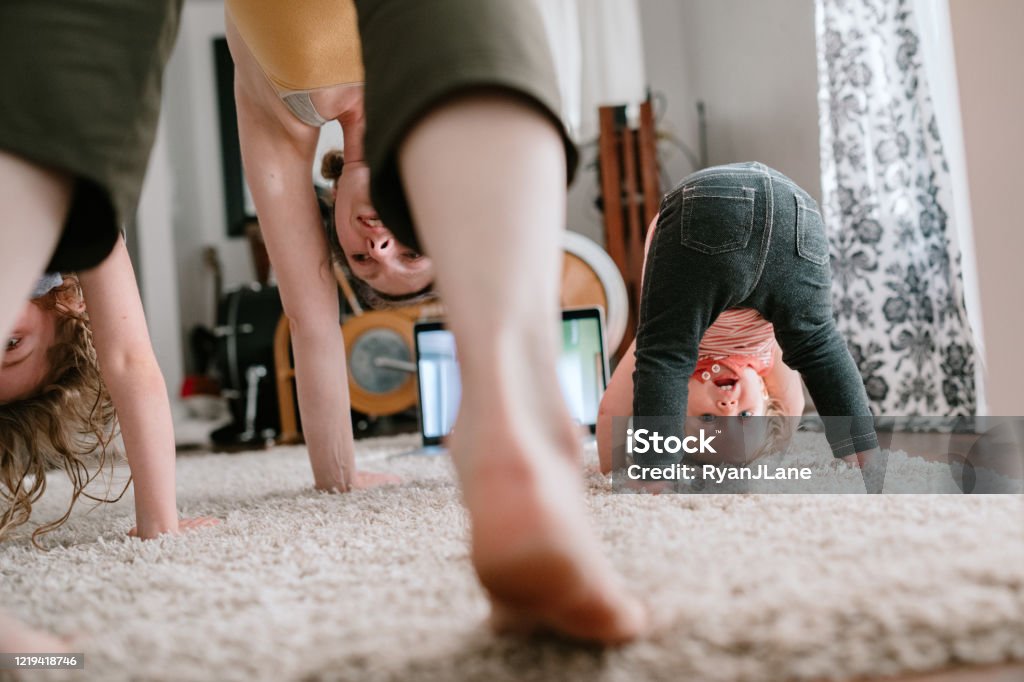 Family Doing Home Workout Online Class A mother does a virtual exercise class with her daughters in their living room.  Part of the regular routine or the new normal with social distancing and Covid-19. Family Stock Photo
