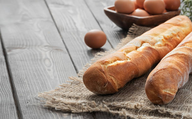 Fresh french baguette made from white flour next to chicken eggs and flour, ingredients for baking. Bread located on burlap, rustic dark wooden background. Close-up, copy space for text.
