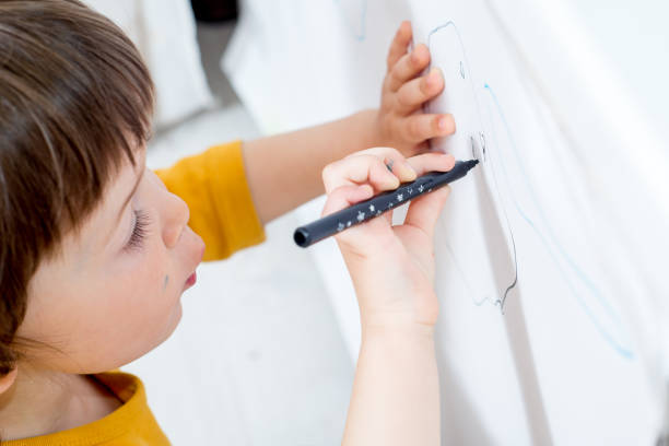 istock little child draws on a white board with a felt-tip pen. Home activities in self-isolation 1219426408