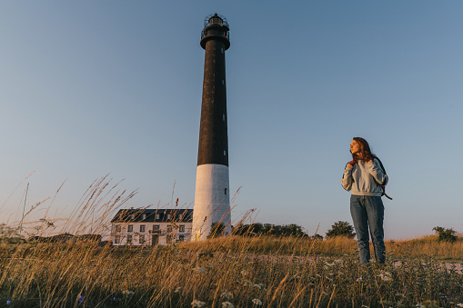 Young Caucasian woman walking near the lighthouse on the beach at sunset