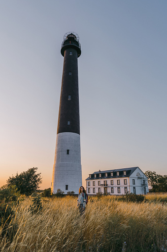 Young Caucasian woman walking near the lighthouse on the beach at sunset