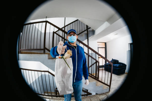 Man delivering groceries during lockdown Man with protective gloves and face mask at door of apartment delivering fresh food in bag during covid-19 coronavirus crisis curfew quarantine. peep hole stock pictures, royalty-free photos & images