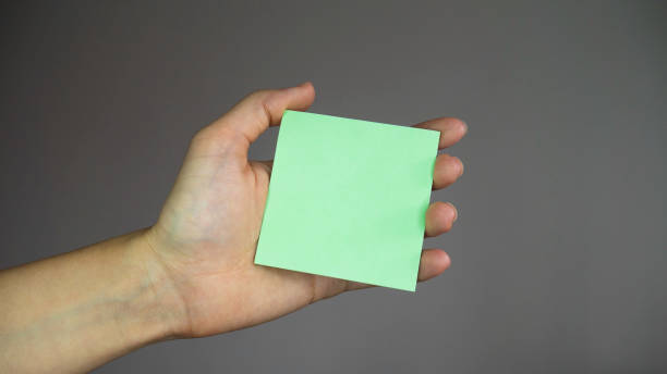 istock Hand holding a blank sticker. Square paper with space for text in the hand. Sticky note with in a hand. 1219430196