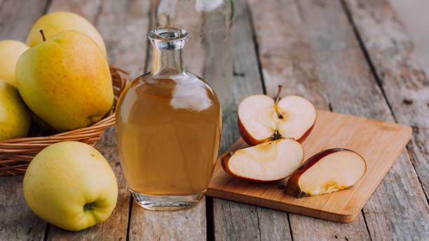 vinagre orgânico de maçã em jarro de vidro com maçãs vermelhas e amarelas frescas maduras na mesa rústica de madeira. conceito de alimentos orgânicos saudáveis. - red jug - fotografias e filmes do acervo