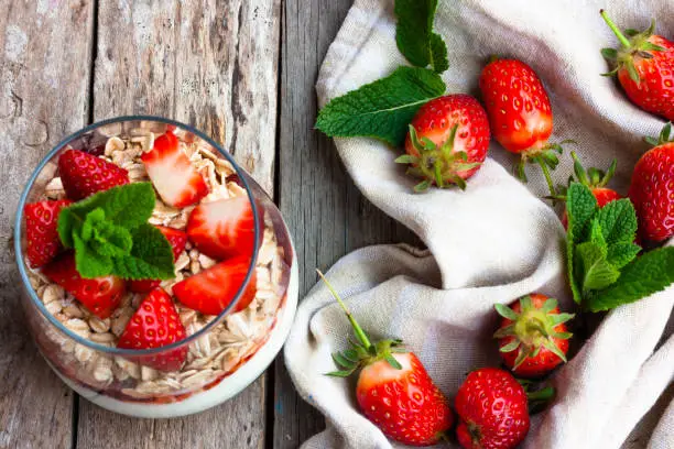 Yogurt with muesli and fresh strawberries for healthy breakfast or snack. Strawberry dessert parfait with yogurt and granola on a wooden table and linen kitchen-towel. Healthy and organic nutrition concept. top view. selective focus.