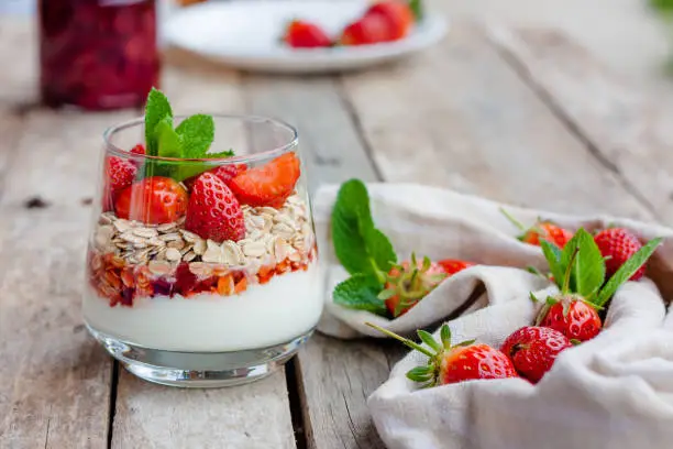 Yogurt with muesli and fresh strawberries for healthy breakfast or snack. Strawberry dessert parfait with yogurt and granola on a wooden table and linen kitchen-towel. Healthy and organic nutrition concept. Selective focus.