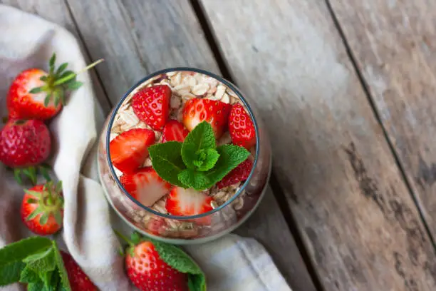 Yogurt with muesli and fresh strawberries for healthy breakfast or snack. Strawberry dessert parfait with yogurt and granola on a wooden table and linen kitchen-towel. Healthy and organic nutrition concept. top view. selective focus.