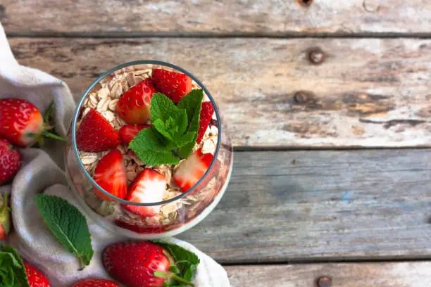 Yogurt with muesli and fresh strawberries for healthy breakfast or snack. Strawberry dessert parfait with yogurt and granola on a wooden table and linen kitchen-towel. Healthy and organic nutrition concept. top view. selective focus.