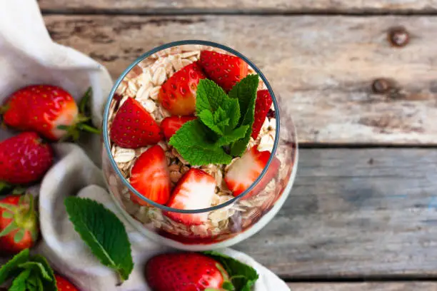 Yogurt with muesli and fresh strawberries for healthy breakfast or snack. Strawberry dessert parfait with yogurt and granola on a wooden table and linen kitchen-towel. Healthy and organic nutrition concept. top view. selective focus.