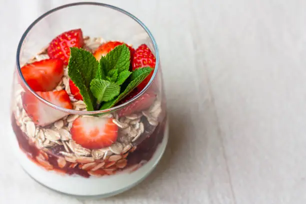 Yogurt with muesli and fresh strawberries for healthy breakfast or snack. Strawberry dessert parfait with yogurt and granola on a wooden table and linen kitchen-towel. Healthy and organic nutrition concept. top view. selective focus.