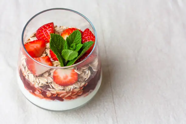 Yogurt with muesli and fresh strawberries for healthy breakfast or snack. Strawberry dessert parfait with yogurt and granola on a wooden table and linen kitchen-towel. Healthy and organic nutrition concept. top view. selective focus.