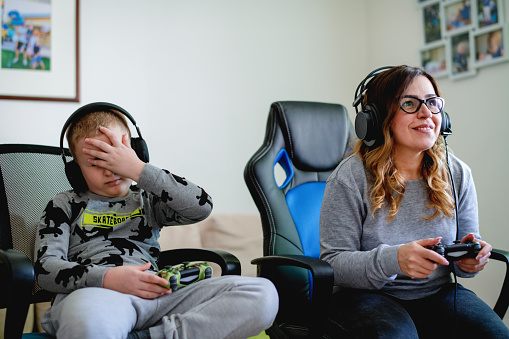Young Caucasian mother and her son spending their free time playing video games and having fun.