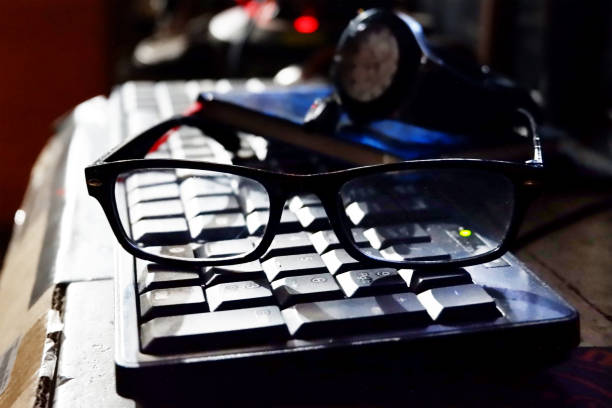 istock glasses with black clear glass frames above the computer keyboard with a background blue watch 1219440591