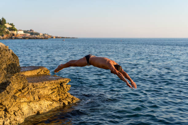 istock Muscular athlete jumping off a rocky beach into water 1219443005