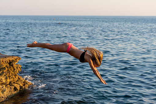 Handsome young woman diving into the sea. Pink and black bikini, blond hair.