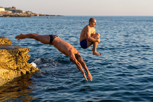Two guys diving from a cliff. Muscular guys, bomb jump and swimming trunks