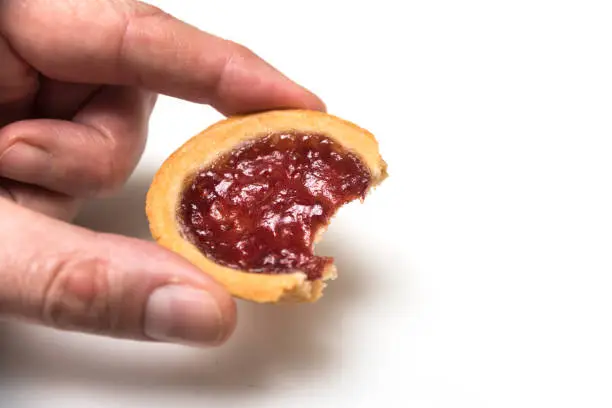 Closeup of crunched mini tartlets with strawberry jam in hand on white background