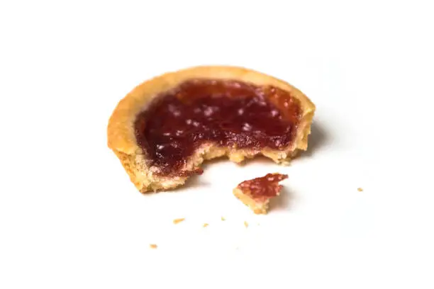 Closeup of one crunched mini tartlet with strawberry jam on white background