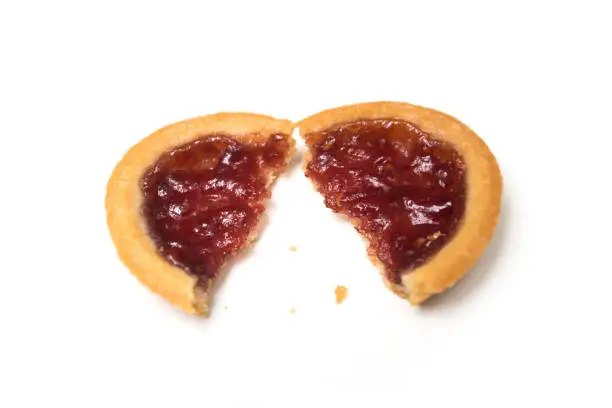 Closeup of crunched mini tartlet with strawberry jam on top view on white background