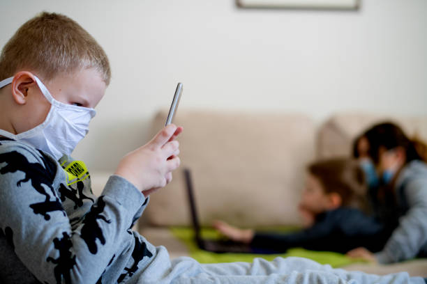 istock Mother and sons at home sofa with mask using technology at quarantine isolation 1219447435