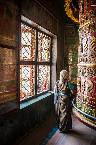 Bodnath, Kathmandu, Nepal- September 09 2017: Tibetan old woman praying and reciting mantras around a big prayer wheel inside a prayer room at Bodnath, in Kathmandu, Nepal.