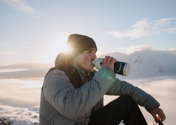 Man drinks water on snowy mountain ridge at sunrise