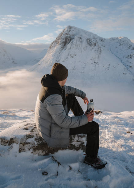 istock Man drinks water on snowy mountain ridge at sunrise 1219453221