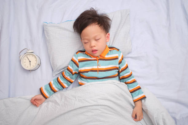 アジア3 - 4歳の幼児の男の子の子供は、目覚まし時計で背中に寝て、昼寝をして、子供の発達の概念で睡眠の重要性 - 3 4 years ストックフォトと画像