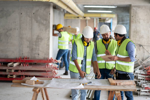 istock Team of three people at a construction site discussing the project while woman looks at blueprint 1219457517