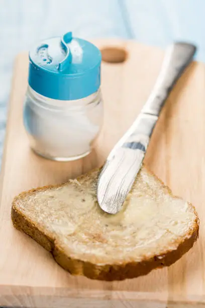 Flat lay butter spread on bread with knife and saltshaker served on a wooden board.