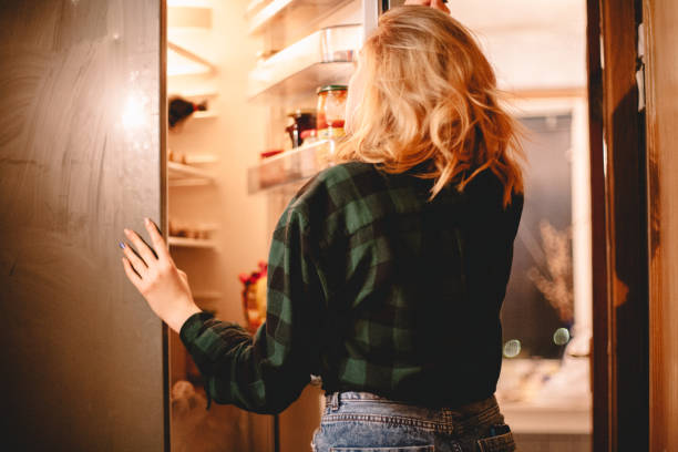 istock Young woman looking in open refrigerator 1219459171