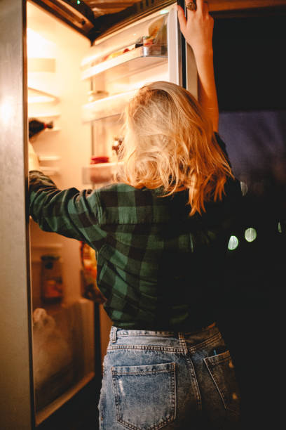 istock Young woman looking in open refrigerator 1219459172