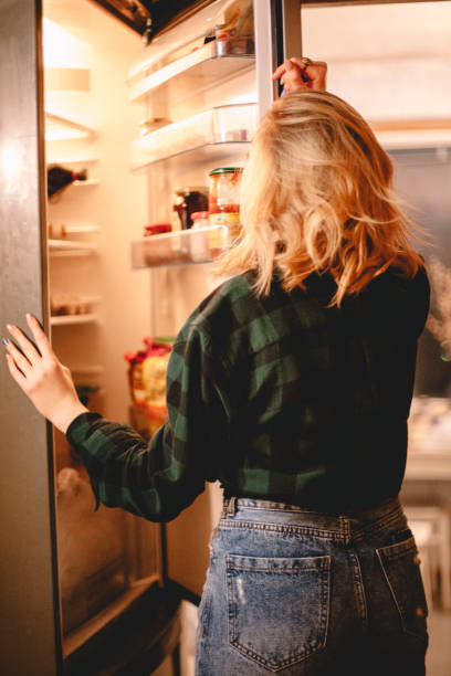 istock Young woman looking in open refrigerator 1219459173