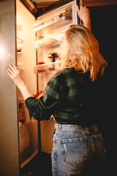istock Young woman looking in open refrigerator 1219459177
