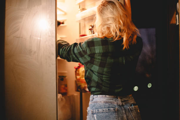 istock Young woman looking in open refrigerator 1219459178