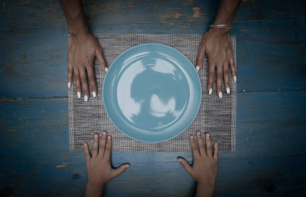 Dish symmetrical composition of four hands on a blue table and empty dish or plate zenith view poverty photos stock pictures, royalty-free photos & images