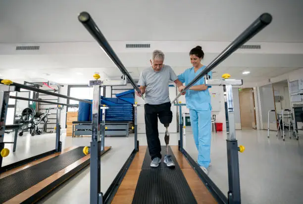 Disabled senior man wearing a prosthetic and doing physical therapy walking on a treadmill - healthcare and medicine