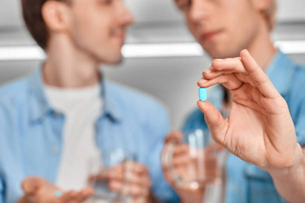 Homosexual Relationship. Gay couple at home holding pre-exposure prophylaxis pill close-up Young gay couple at home standing atitchen holding cups of water and blue pill pre-exposure prophylaxis close-up hiv photos stock pictures, royalty-free photos & images