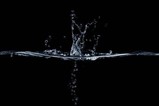 Water Splash Detail Side view close-up of the abstract shapes of light against splashing water for use as a design element or background. water on black surface stock pictures, royalty-free photos & images