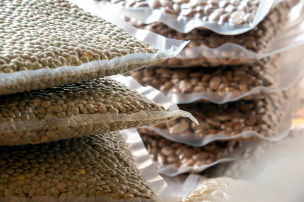 Horizontal photograph of stacks of 1 pound vacuum sealed bags of dried pinto beans, lentils, elbow macaroni noodles and oatmeal sitting on a table.