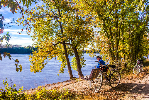 Ciclista masculino mayor descansando junto al río en un agradable día de otoño photo
