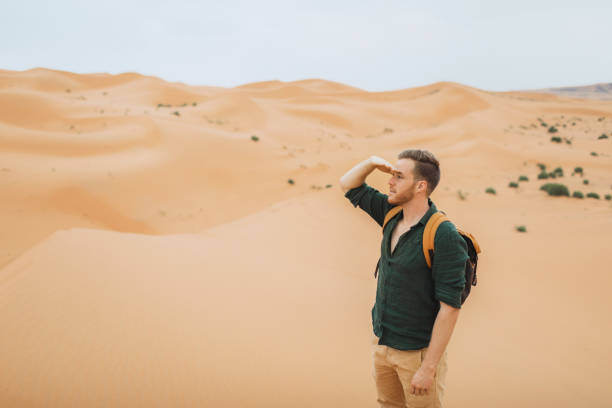 istock Man backpacker travel in Morocco, Sahara desert.  Looking forward and explore african nature, sand dunes around. 1219480809