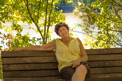 Attractive middle aged woman sitting on a wooden bench in the fall, smiling; river in the background; Missouri, Midwest