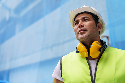 Thoughtful blue collar worker at a construction site looking up wearing protective workwear