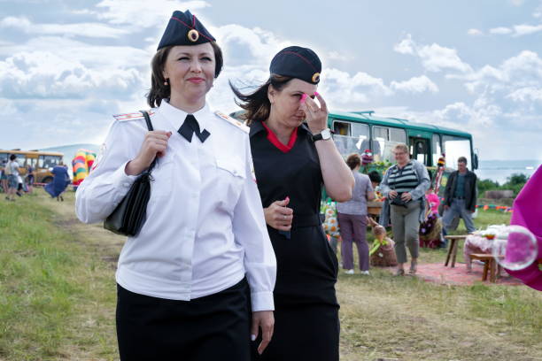 경찰 제복을 입은 두 명의 미소 짓는 젊은 여성이 음악과 민족 축제 카라태그에서 근무하는 동안 길을 따라 걷고 있습니다. - russian culture women spy russia 뉴스 사진 이미지