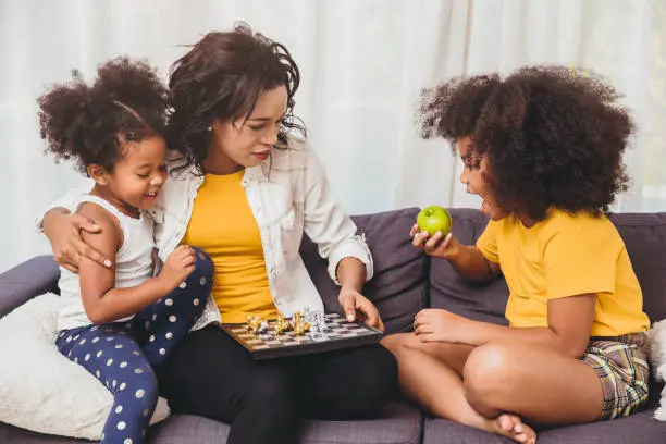 Single mom good care, teaching her childs to be genius and clever little girls learning to play chess boardgame eating fruit for healthy.