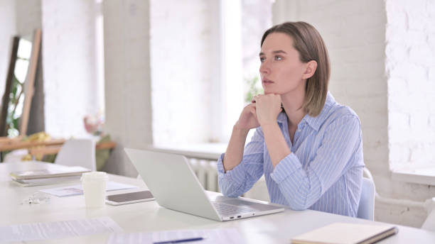 istock Young Professional Woman Thinking and Working on Laptop 1219498101